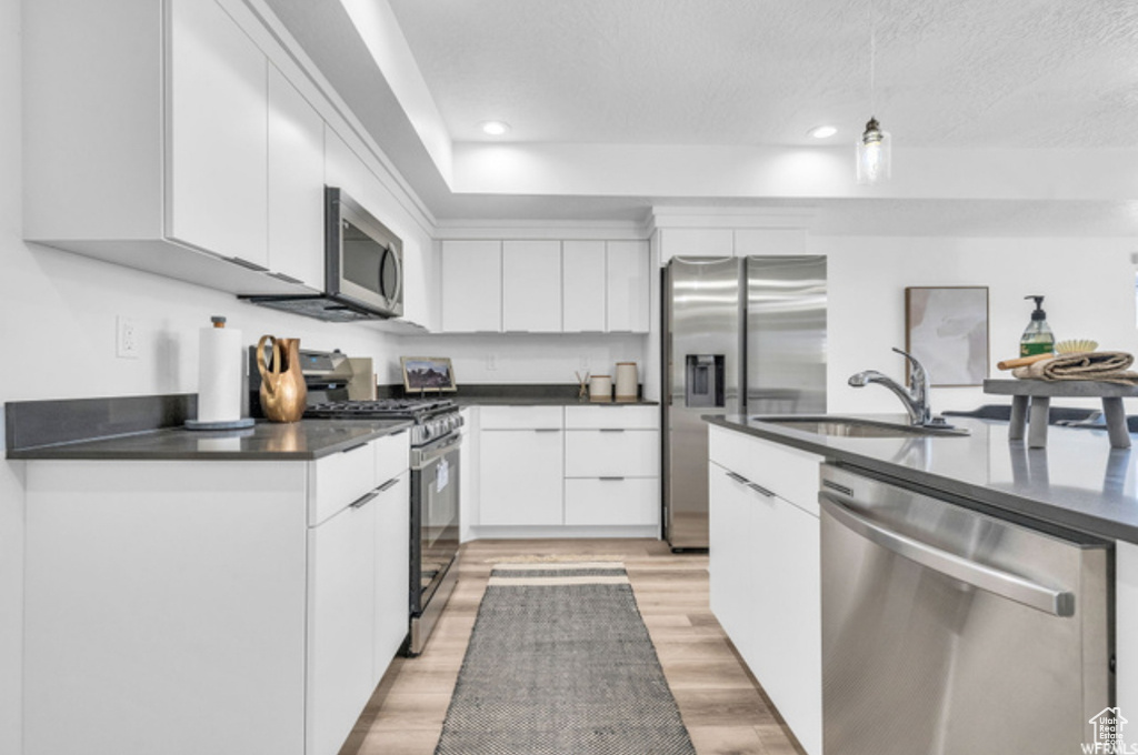 Kitchen featuring hanging light fixtures, white cabinetry, appliances with stainless steel finishes, sink, and light hardwood / wood-style floors