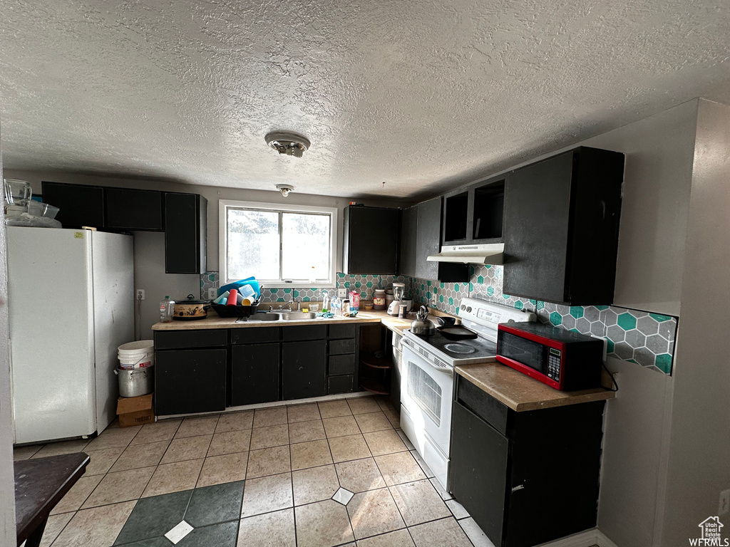 Kitchen featuring white appliances, sink, light tile floors, tasteful backsplash, and a textured ceiling