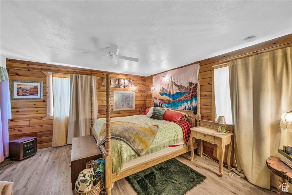 Bedroom featuring hardwood / wood-style flooring, wooden walls, and ceiling fan