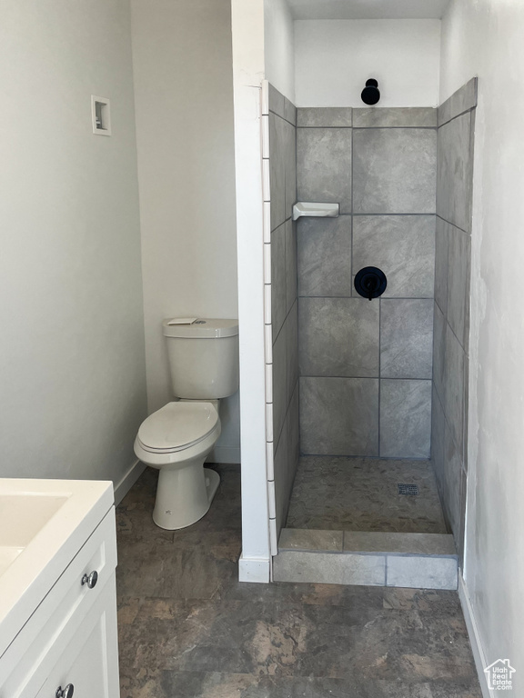 Bathroom with tiled shower, toilet, tile flooring, and vanity