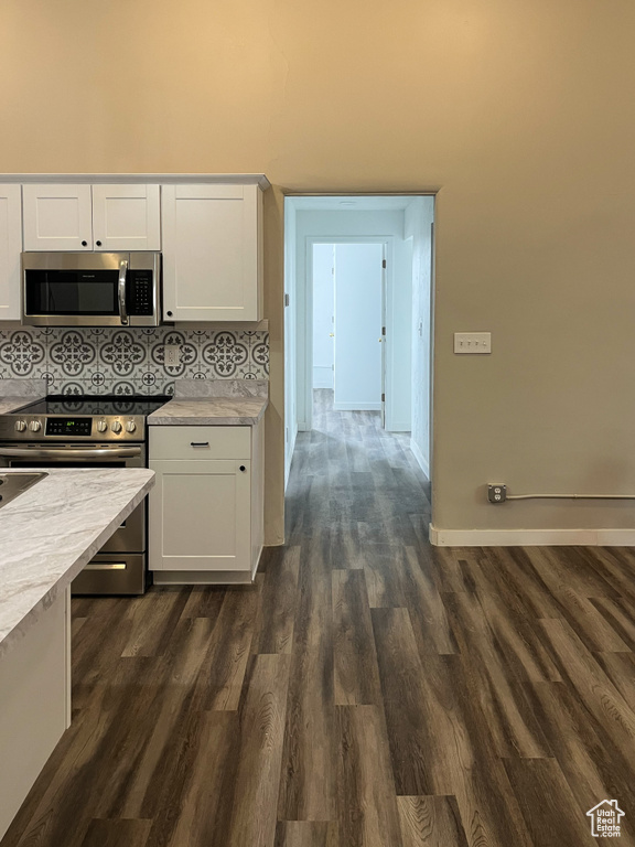 Kitchen with tasteful backsplash, white cabinetry, stainless steel appliances, and dark wood-type flooring