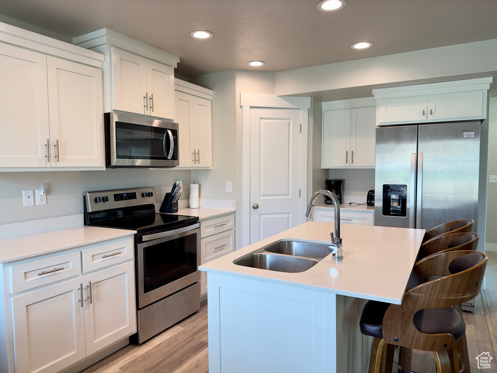 Kitchen with stainless steel appliances, an island with sink, white cabinets, sink, and light wood-type flooring
