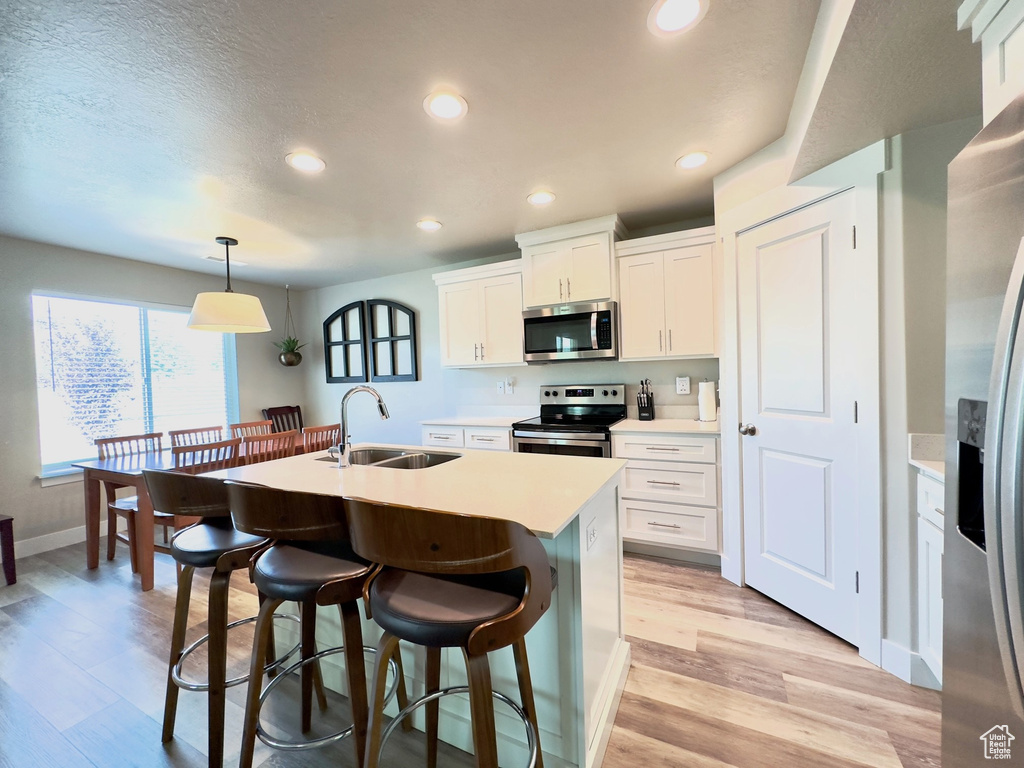 Kitchen featuring appliances with stainless steel finishes, an island with sink, sink, hanging light fixtures, and light hardwood / wood-style flooring