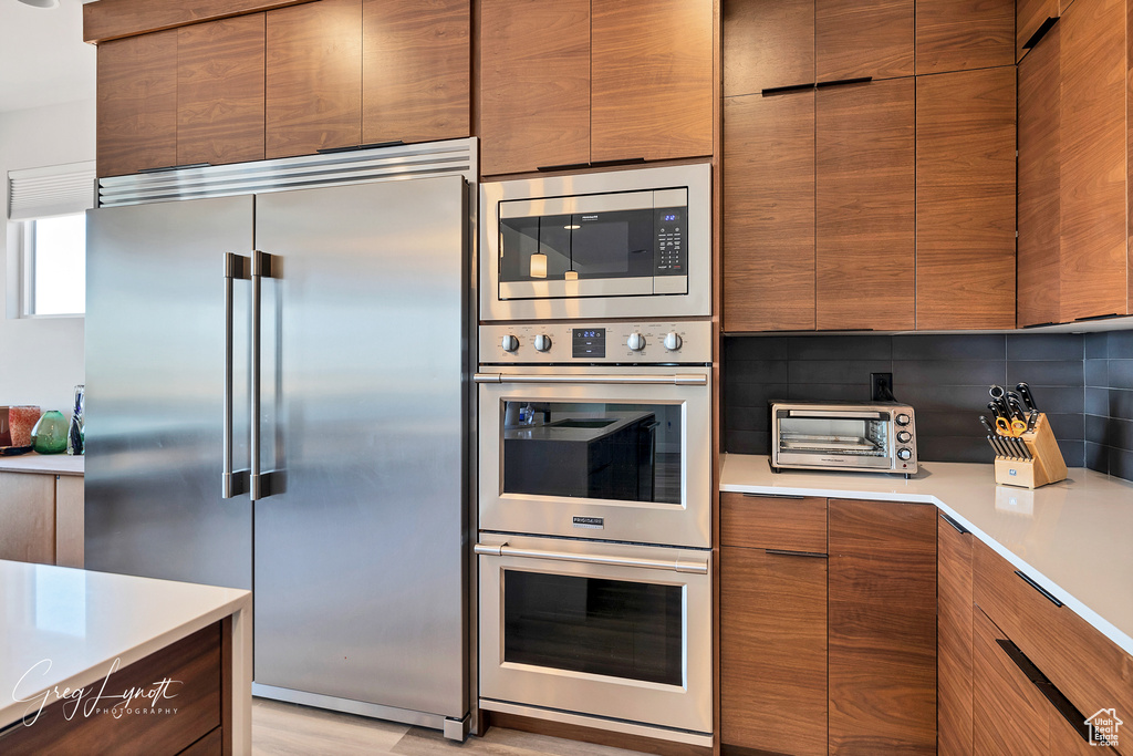 Kitchen featuring built in appliances, light hardwood / wood-style floors, and backsplash