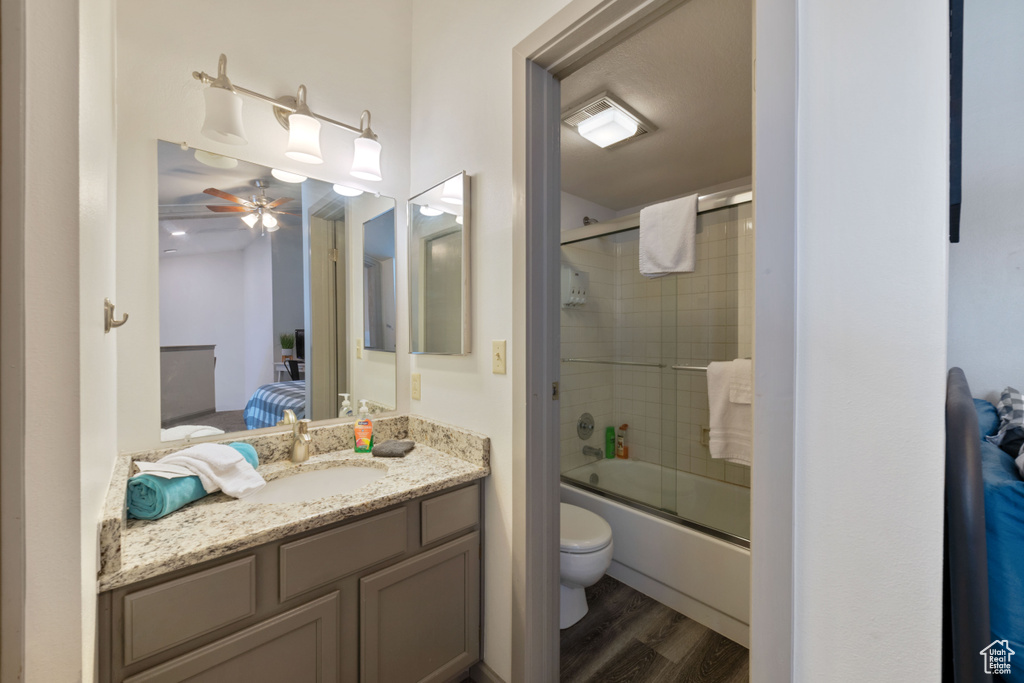 Full bathroom featuring vanity, bath / shower combo with glass door, hardwood / wood-style flooring, toilet, and ceiling fan