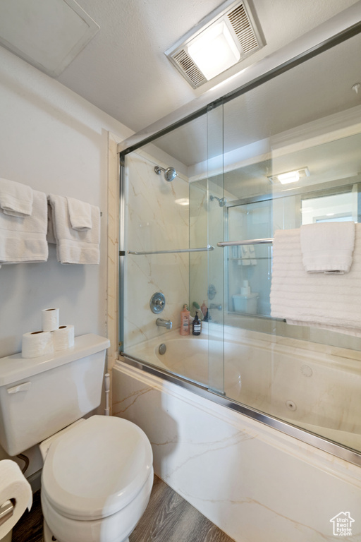 Bathroom featuring toilet, shower / bath combination with glass door, and hardwood / wood-style flooring