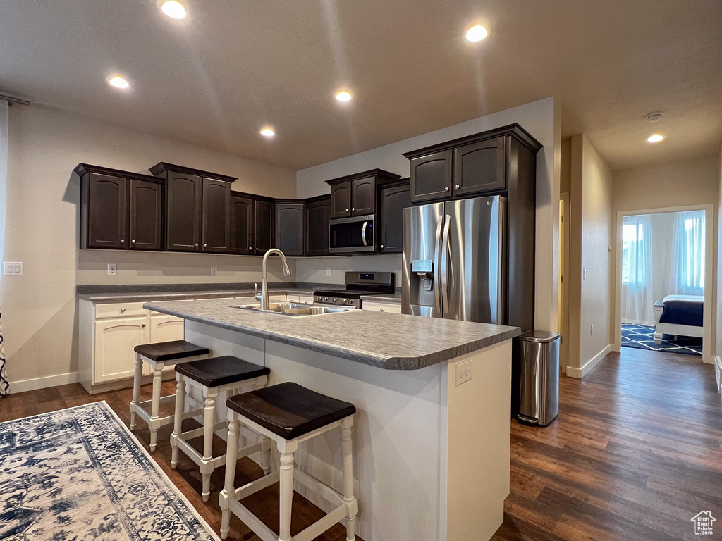 Kitchen with sink, appliances with stainless steel finishes, a center island with sink, dark brown cabinetry, and dark hardwood / wood-style flooring