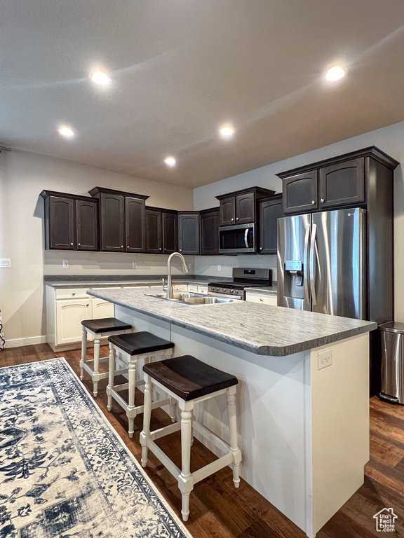 Kitchen featuring appliances with stainless steel finishes, dark brown cabinets, dark hardwood / wood-style flooring, and a center island with sink