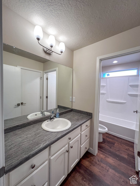 Full bathroom with wood-type flooring, large vanity, toilet, washtub / shower combination, and a textured ceiling