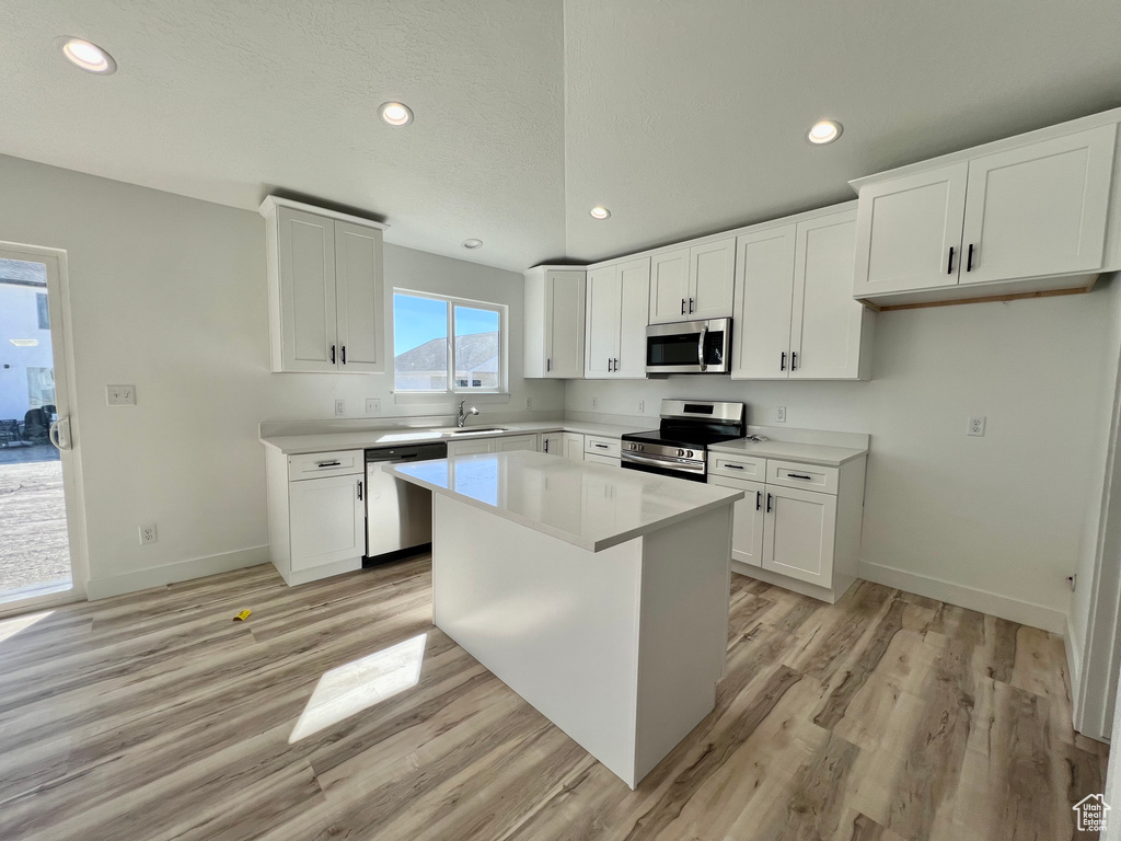 Kitchen with a center island, white cabinets, light hardwood / wood-style flooring, stainless steel appliances, and sink