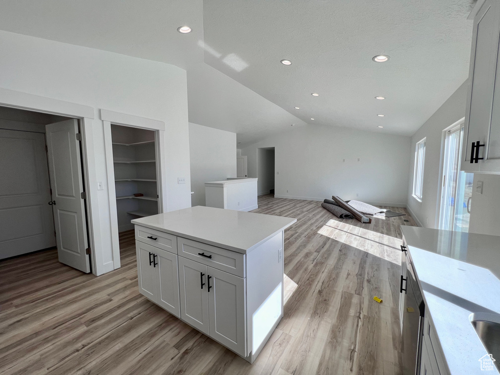 Kitchen with white cabinets, lofted ceiling, light hardwood / wood-style flooring, and a center island