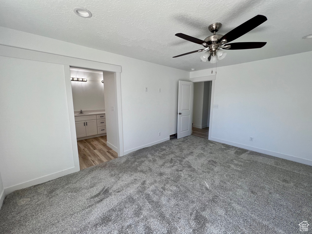 Unfurnished bedroom featuring light carpet, ceiling fan, ensuite bathroom, and a textured ceiling
