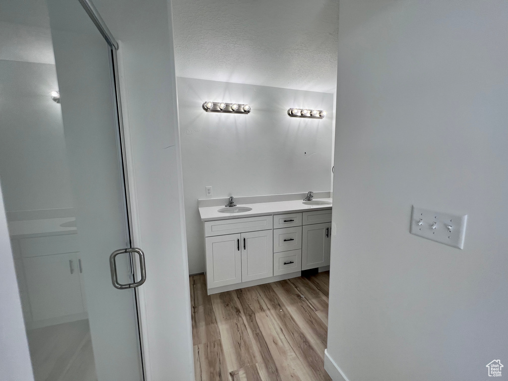 Bathroom with hardwood / wood-style flooring, a shower with shower door, dual bowl vanity, and a textured ceiling