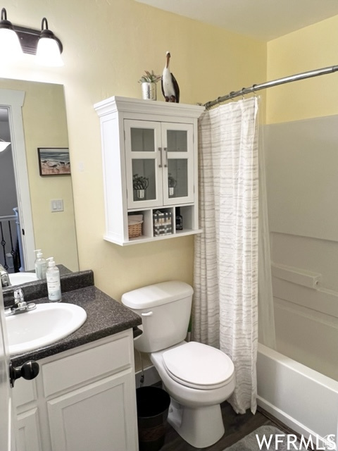Full bathroom with wood-type flooring, shower / tub combo with curtain, vanity, and toilet
