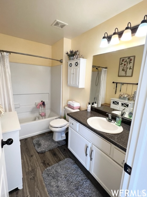 Full bathroom with shower / bathtub combination with curtain, toilet, hardwood / wood-style floors, and large vanity