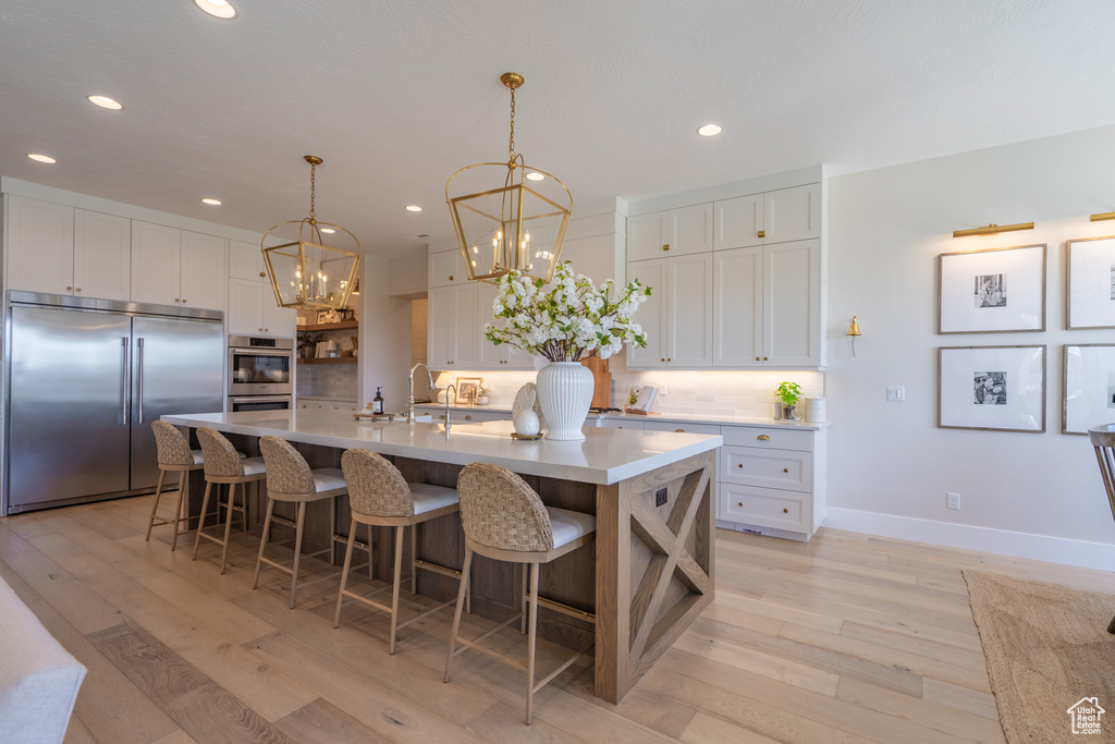 Kitchen featuring appliances with stainless steel finishes, white cabinets, backsplash, a spacious island, and light hardwood / wood-style flooring