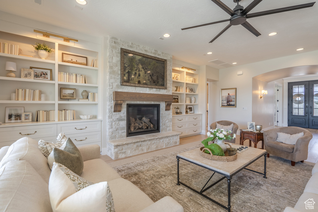 Living room with ceiling fan, a stone fireplace, and built in shelves