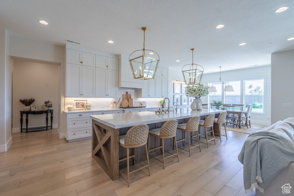Kitchen with a breakfast bar, white cabinets, light hardwood / wood-style flooring, sink, and a center island with sink