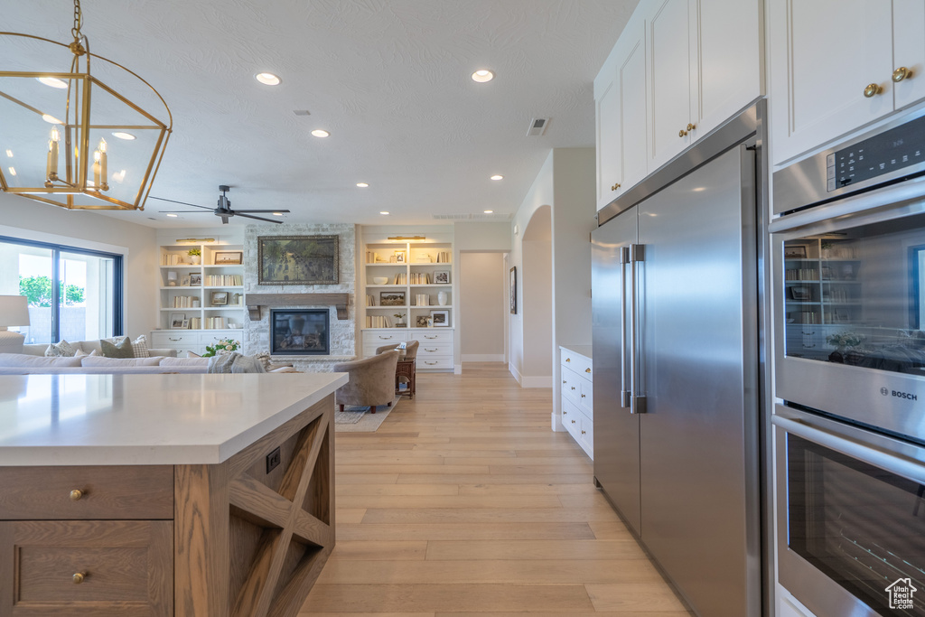 Kitchen with hanging light fixtures, a large fireplace, white cabinetry, appliances with stainless steel finishes, and light hardwood / wood-style floors