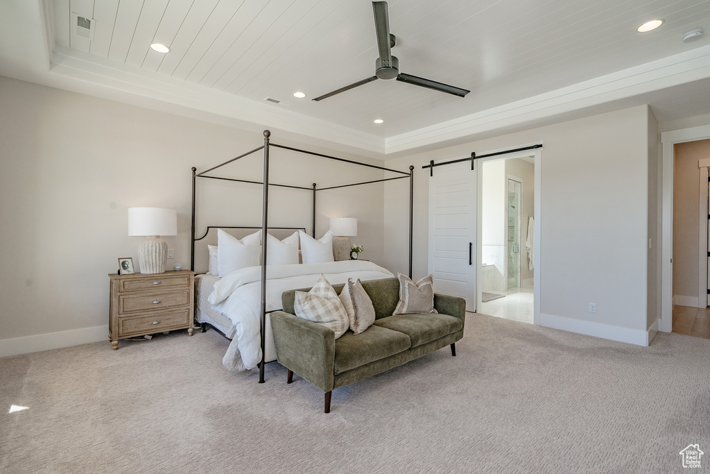 Carpeted bedroom with connected bathroom, ceiling fan, a barn door, and a tray ceiling