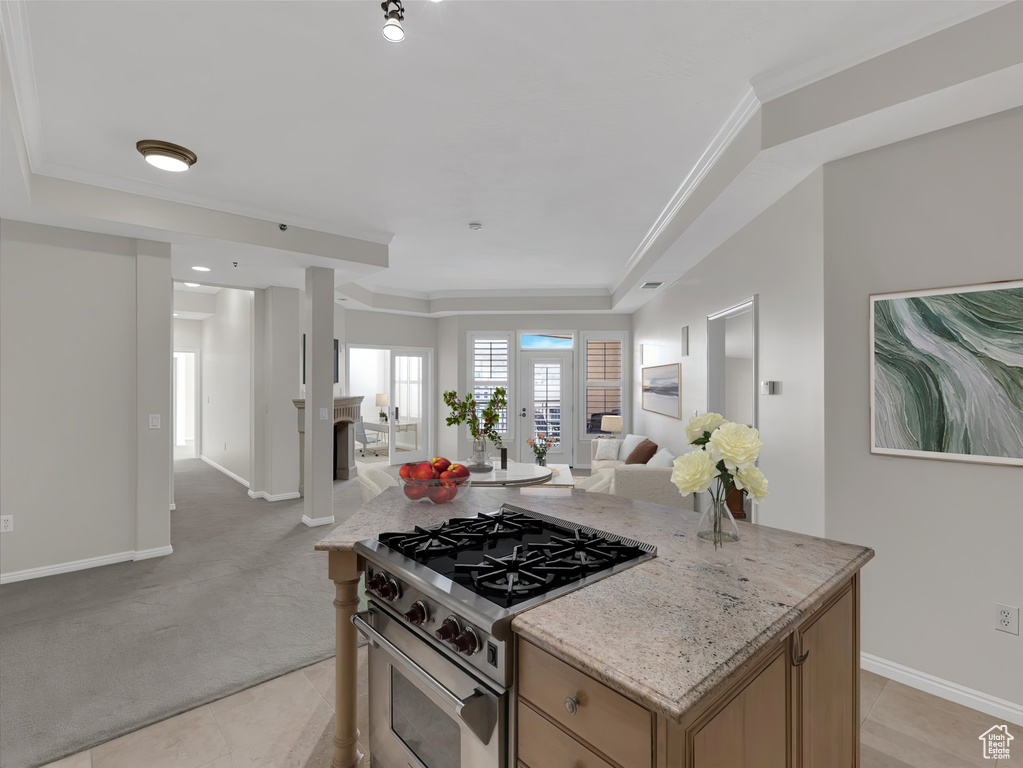 Kitchen featuring light stone countertops, crown molding, high end range, a center island, and light tile floors