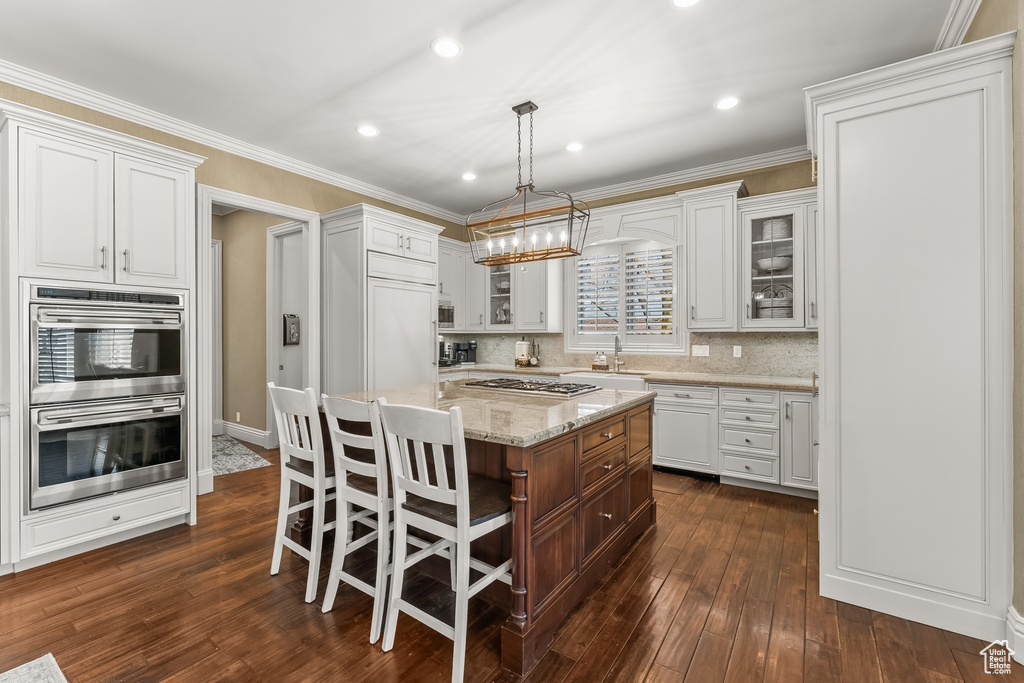 Kitchen with a center island, tasteful backsplash, white cabinetry, crown molding, and dark hardwood / wood-style floors