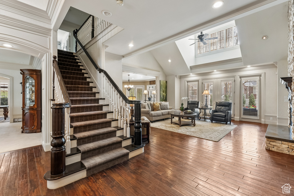 Foyer entrance featuring ceiling fan with notable chandelier, high vaulted ceiling, crown molding, and hardwood / wood-style flooring