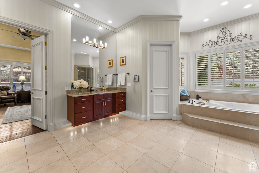 Bathroom featuring tile flooring, vanity, ceiling fan with notable chandelier, and tiled bath