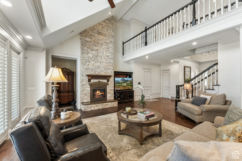 Living room featuring hardwood / wood-style flooring, a stone fireplace, ceiling fan, and high vaulted ceiling