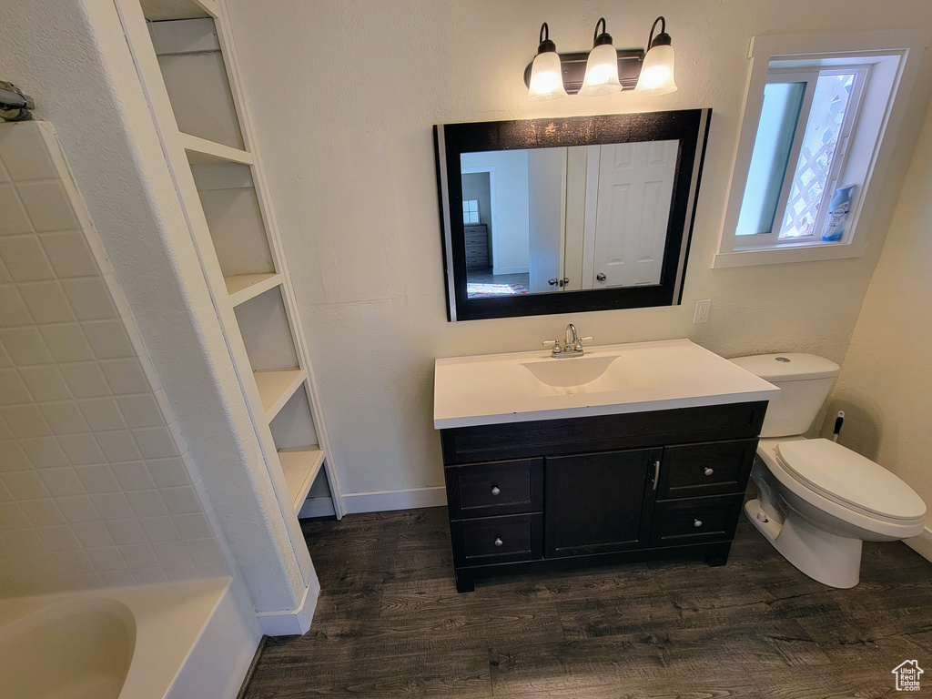 Full bathroom with built in shelves, washtub / shower combination, toilet, wood-type flooring, and vanity