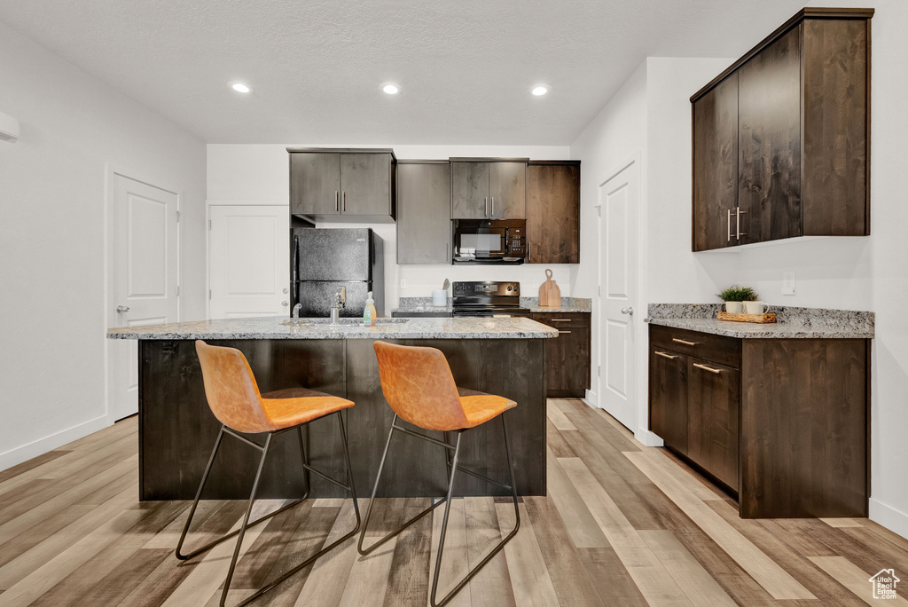 Kitchen featuring light stone counters, a center island with sink, light hardwood / wood-style floors, and black appliances