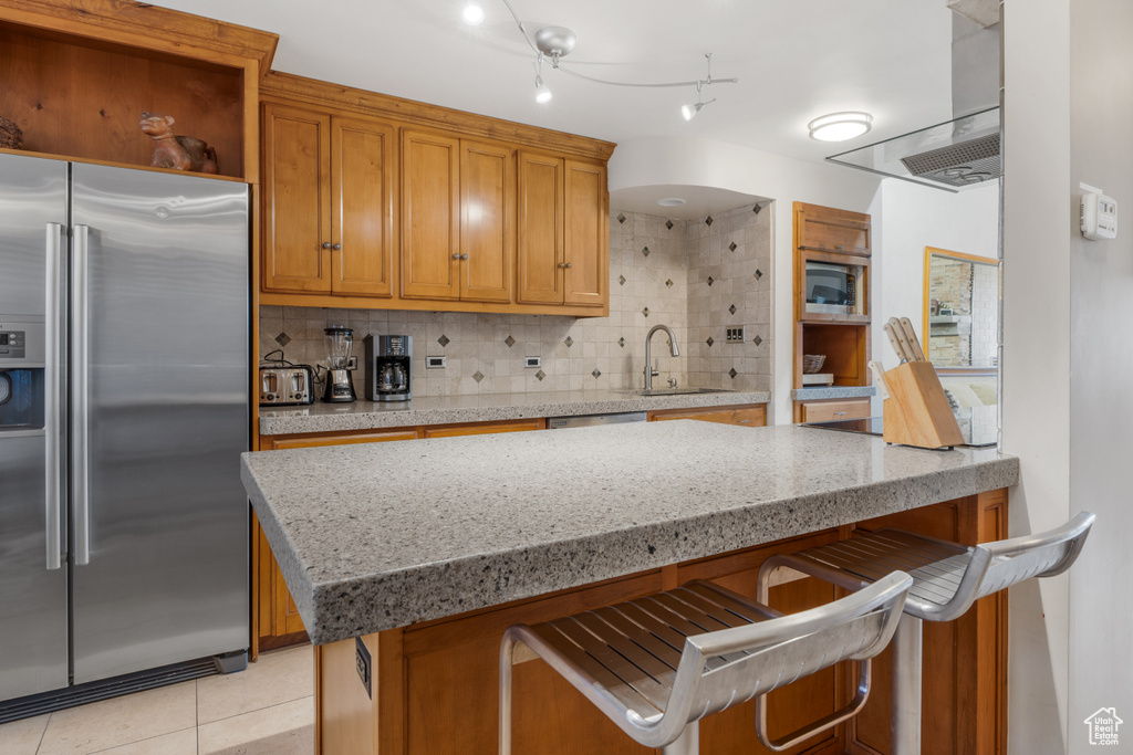 Kitchen with high end refrigerator, sink, light tile floors, and a breakfast bar area