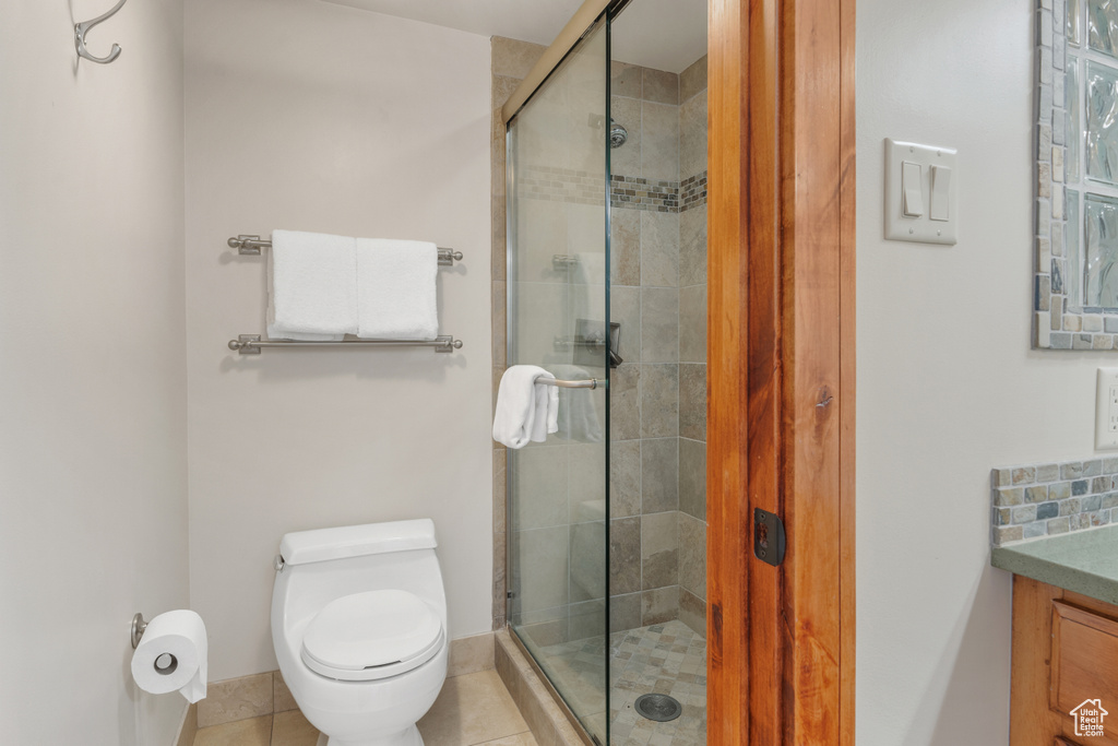 Bathroom featuring a shower with door, vanity, toilet, and tile flooring