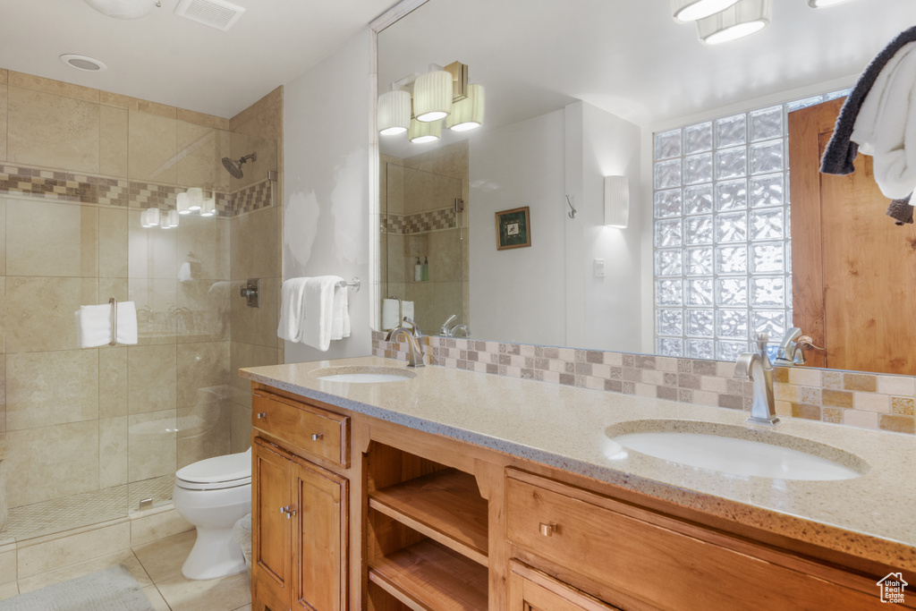 Bathroom with large vanity, a shower with shower door, dual sinks, tasteful backsplash, and toilet