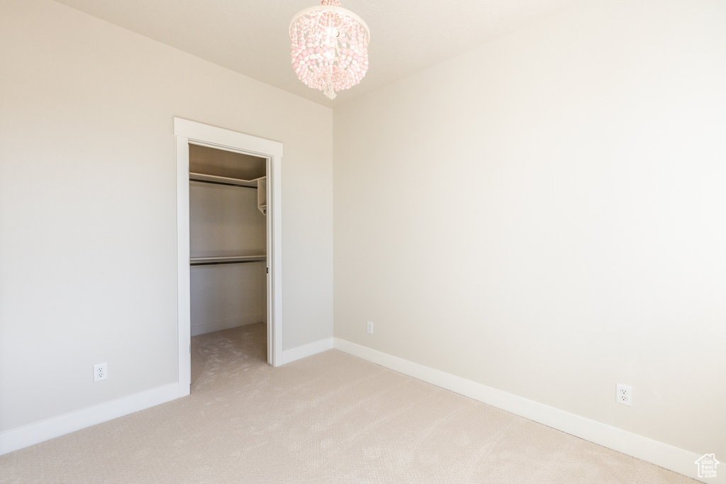 Unfurnished bedroom with a closet, a spacious closet, light carpet, and a chandelier
