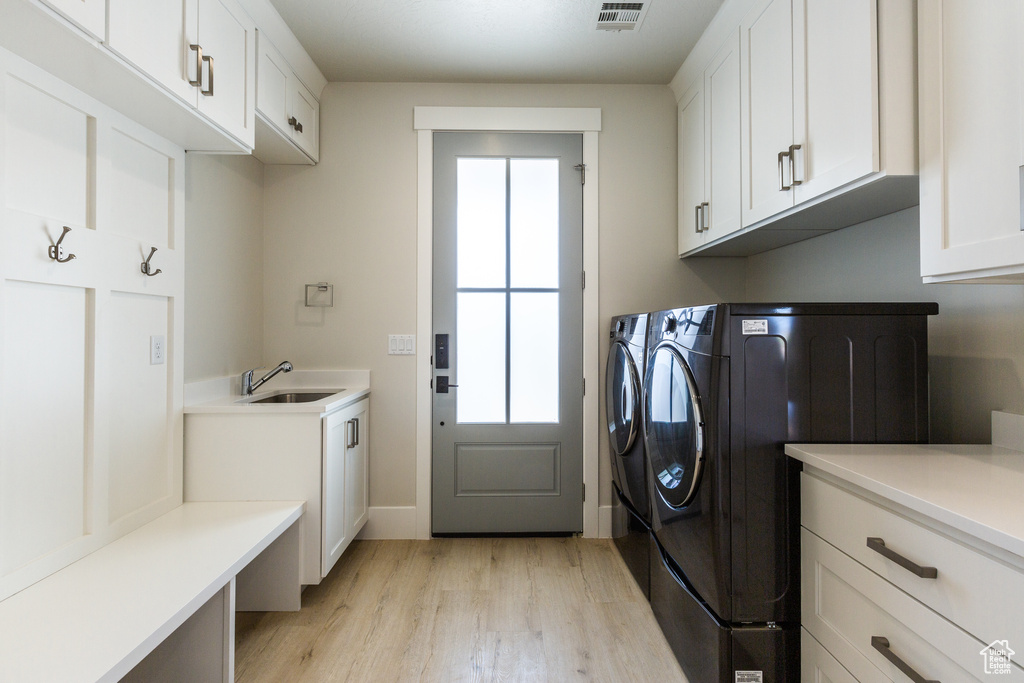 Clothes washing area featuring sink, light hardwood / wood-style floors, cabinets, and plenty of natural light