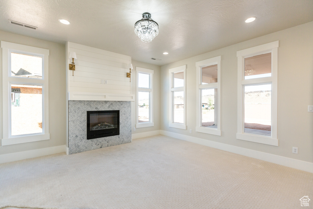 Unfurnished living room with a chandelier, a tiled fireplace, and light carpet