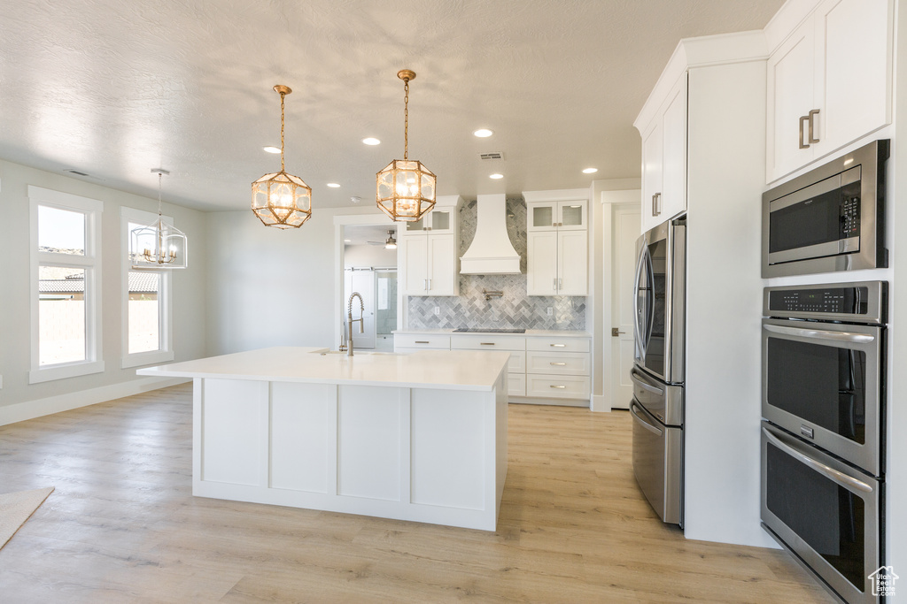 Kitchen featuring premium range hood, stainless steel appliances, tasteful backsplash, white cabinets, and light wood-type flooring