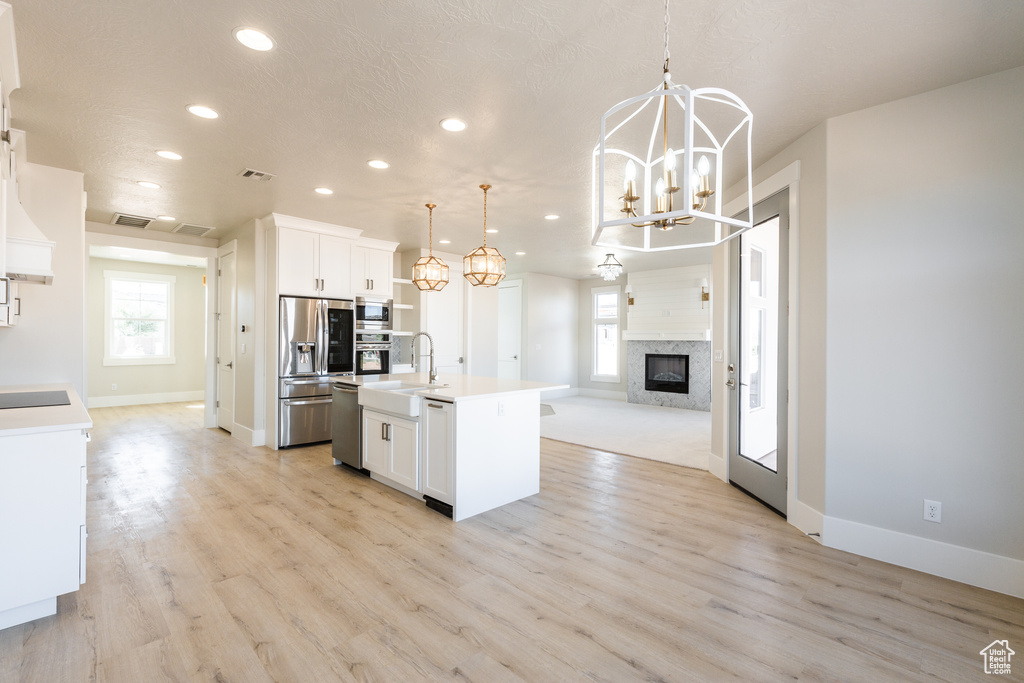 Kitchen featuring appliances with stainless steel finishes, decorative light fixtures, white cabinetry, and light wood-type flooring