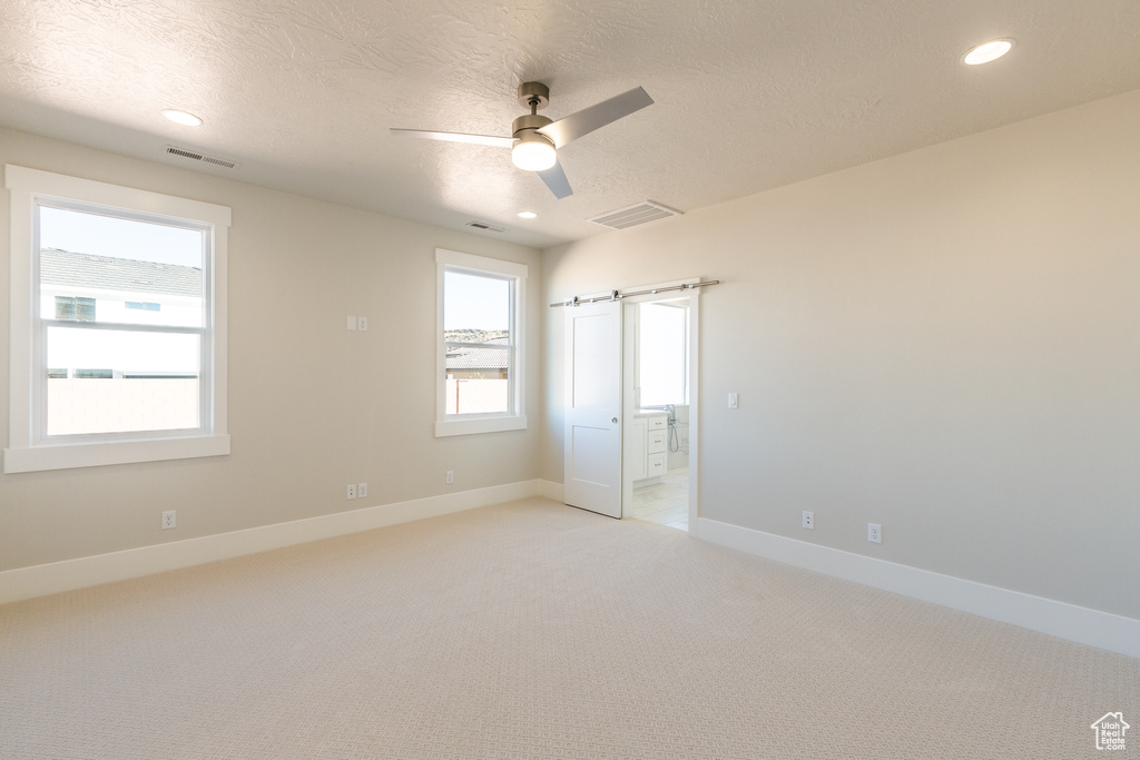 Spare room with light colored carpet, ceiling fan, and a barn door