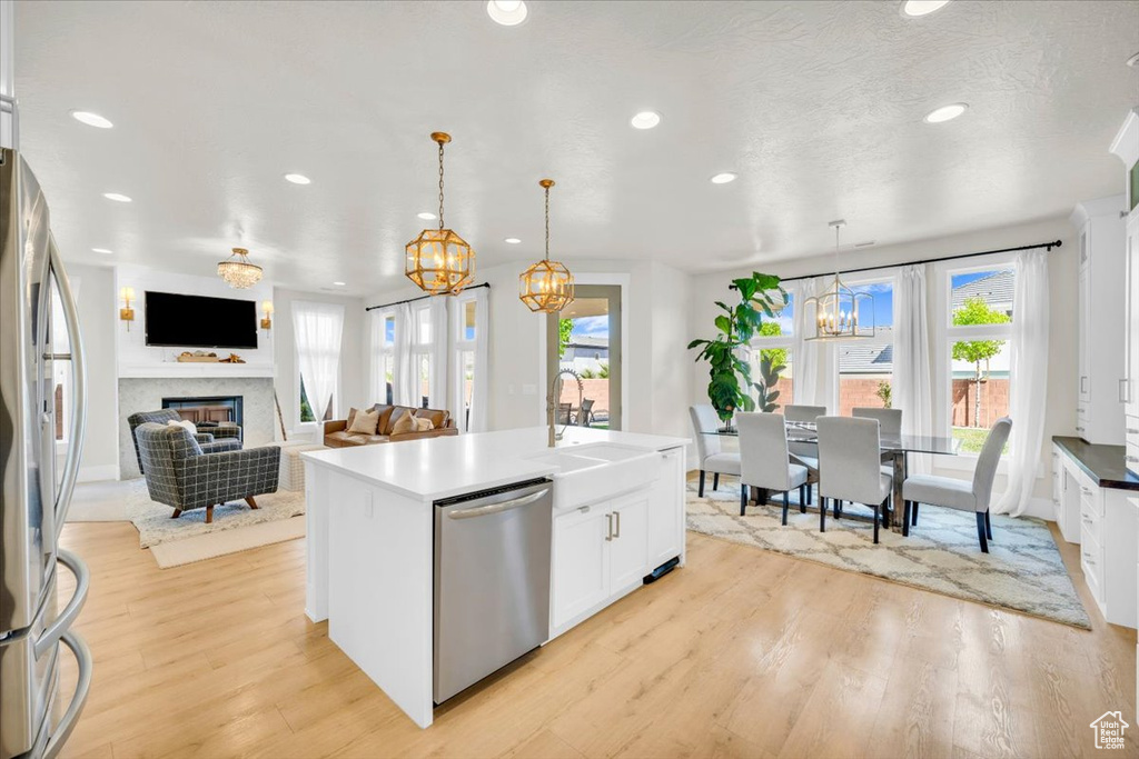 Kitchen with white cabinets, light hardwood / wood-style floors, appliances with stainless steel finishes, and pendant lighting