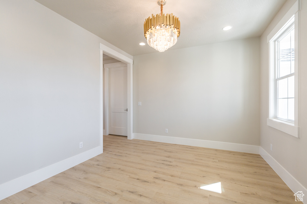 Empty room featuring light hardwood / wood-style flooring, a notable chandelier, and plenty of natural light