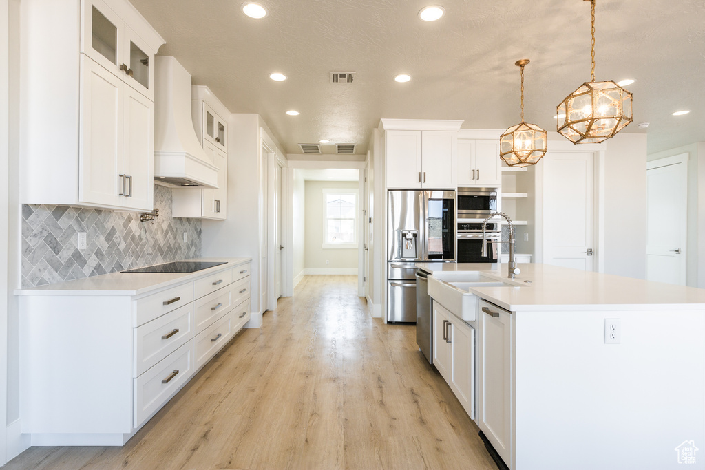 Kitchen with custom range hood, hanging light fixtures, light hardwood / wood-style floors, and white cabinetry