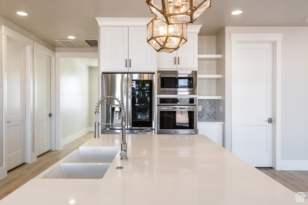 Kitchen featuring hanging light fixtures, stainless steel appliances, light hardwood / wood-style floors, and an inviting chandelier