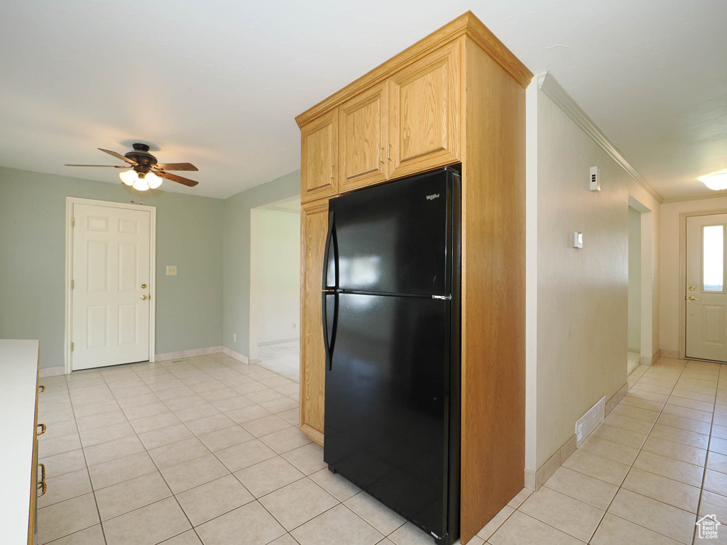 Kitchen featuring light brown cabinets, ceiling fan, light tile floors, black fridge, and crown molding