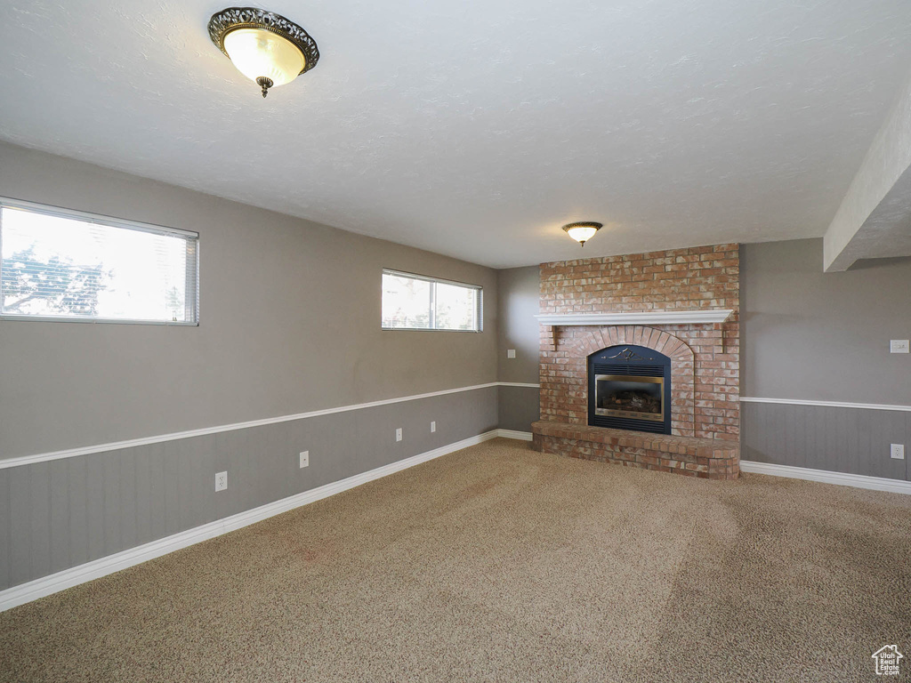 Unfurnished living room featuring brick wall, a brick fireplace, and carpet flooring