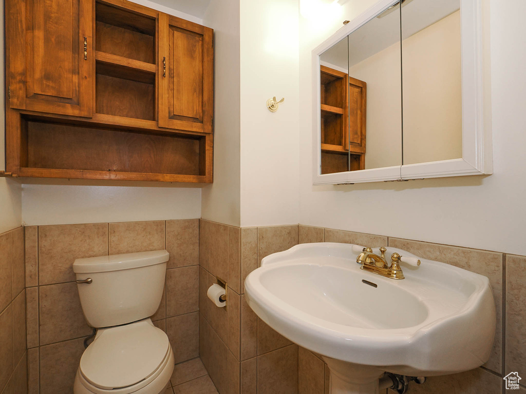 Bathroom with toilet, tile flooring, tile walls, and sink