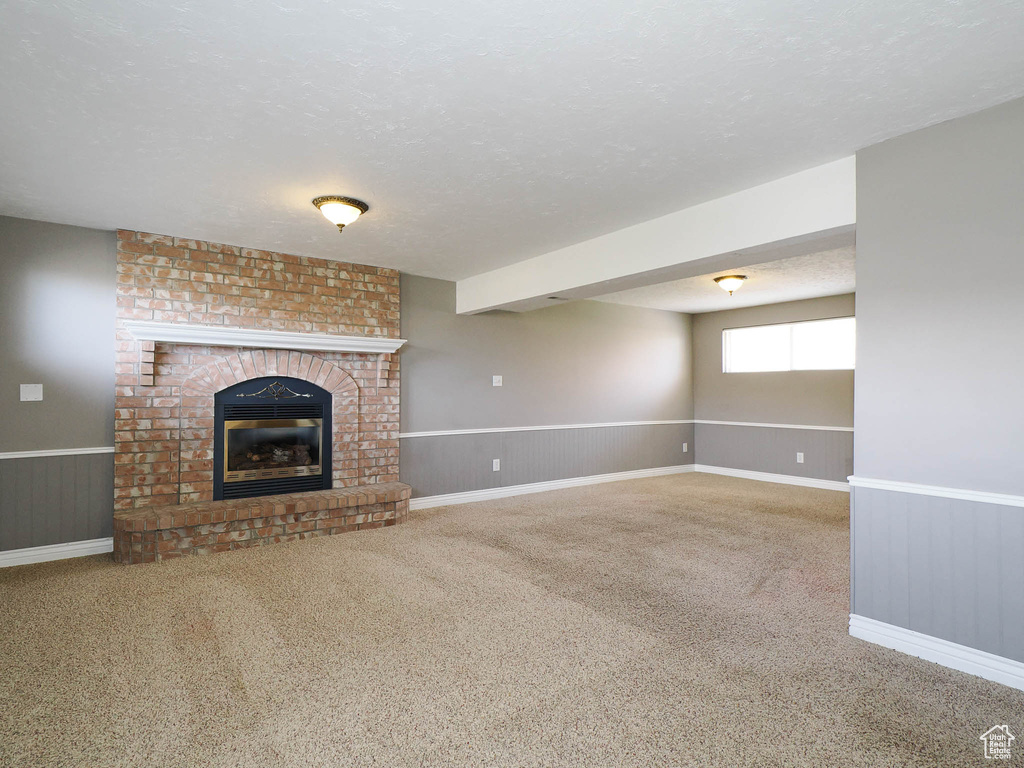 Unfurnished living room featuring brick wall, carpet, a fireplace, and a textured ceiling