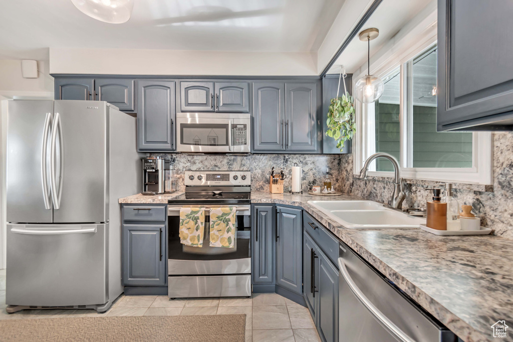 Kitchen featuring hanging light fixtures, light tile flooring, backsplash, stainless steel appliances, and sink