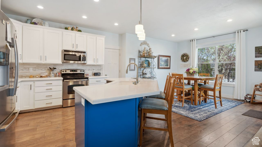 Kitchen featuring hanging light fixtures, light wood-type flooring, backsplash, stainless steel appliances, and an island with sink